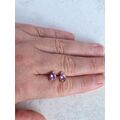 Gold amethyst stud earrings in a hand for scale