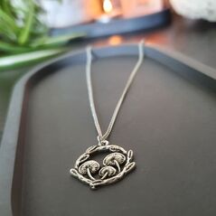 Circular pendant on silver chain depicting 3 mushrooms in a ring of leaves with a textured appearance