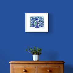 Peacock with Splayed Feathers in Green and Blue Framed in White on a Blue Wall Above a Wooden Drawer Unit
